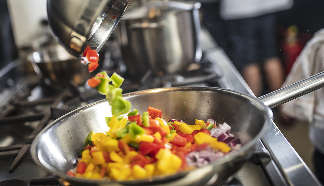 Chef pouring sliced vegetables into pan on stove, close-up
